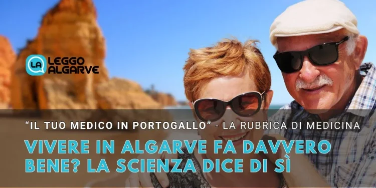 Una coppia di anziani che sembrano vivere bene, indossa occhiali da sole e sorride si trova su una soleggiata spiaggia dell' Algarve in Portogallo con scogliere sullo sfondo. Il testo parla dei benefici di vivere bene in Algarve, citando la scienza.