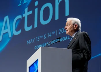 Mattarella parla dal podio sul palco del COTEC 2025 in Portogallo. Dietro di lui, uno schermo blu mostra "Azione", "13 e 14 maggio 2023" e "Coimbra, Portogallo".