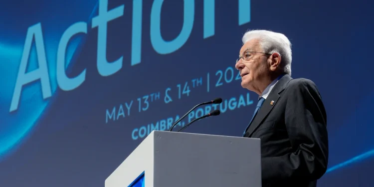 Mattarella parla dal podio sul palco del COTEC 2025 in Portogallo. Dietro di lui, uno schermo blu mostra "Azione", "13 e 14 maggio 2023" e "Coimbra, Portogallo".