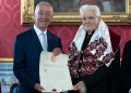 Sergio Mattarella e Marcelo Rebelo de Sousa sono in piedi l'uno accanto all'altro in occasione della consegna del Honoris Causa a Coimbra. Uno, avvolto in una tunica decorata con dettagli rossi e argento, presenta l'attestato. Si trovano in una stanza elegantemente decorata con carta da parati rossa e un dipinto incorniciato all'Università di Coimbra.