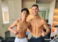 Crisitiano Ronaldo con il figlio a torso nudo sono in piedi, vicini in una palestra, sorridenti verso la telecamera. Entrambi mostrano addominali scolpiti e fanno il gesto del pollice in su. Sullo sfondo si vedono attrezzi da palestra e scaffali.