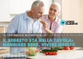 Un uomo e una donna anziani sorridono mentre preparano bene del mangiare sano in una cucina luminosa, dove si può vivere meglio. L'uomo assaggia una fetta di cetriolo. Il testo sovrapposto in italiano, "Mangiare bene, vivere meglio".