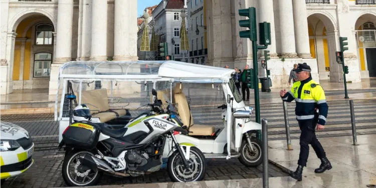 Un tuk-tuks parcheggiato a Lisbona e un poliziotto che si accinge ad emettere la multa. Si vede anche una moto e dei palazzi antichi sullo sfondo.