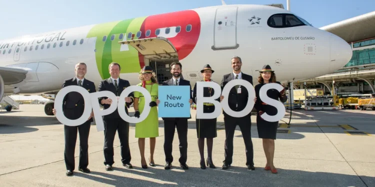Sette membri di equipaggio dei nuovi voli tra il Portogallo e gli USA posano davanti ad un aereo della TAP con alcune lettere in mano. È una giornata di sole con il cielo azzurro sullo sfondo.