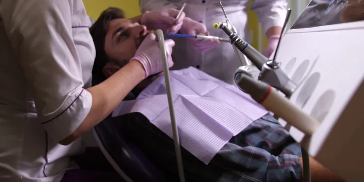 Un uomo mentre si cura da un dentista portoghesi, è sdraiato sulla poltrona del dentista dell SNS, con due medici che lo assistono e attrezzature odontoiatriche visibili in primo piano.