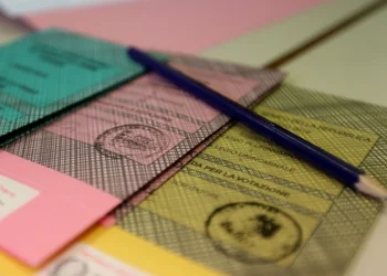 Diverse schede del Referendum 2025 colorate – verde, rosa e giallo – sono disposte su un tavolo probabilmente per italiani residenti all estero. Si vede una matita blu sopra, le schede includono timbri ufficiali e un testo visibile in italiano per i residenti all'estero.