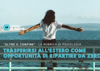 Una ragazza con una maglietta bianca di spalle decisa a trasferirsi all estero ha le braccia allargate per ripartire da una balaustra. Sullo sfondo si vede il mare una scogliera e alcune montagne oltre un cielo azzurro.