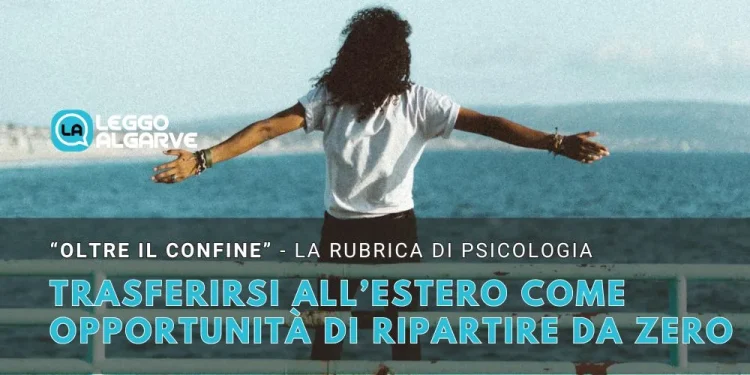 Una ragazza con una maglietta bianca di spalle decisa a trasferirsi all estero ha le braccia allargate per ripartire da una balaustra. Sullo sfondo si vede il mare una scogliera e alcune montagne oltre un cielo azzurro.