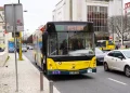 Un autobus dei trasporti urbano giallo sulla linea 717 per Fetais percorre una strada di Lisbona, in Portogallo, tra auto e pedoni, attualmente lo si deve pagare, ma in futuro potrebbe essere gratuiti. Sono visibili edifici, un teatro e cartelli stradali.