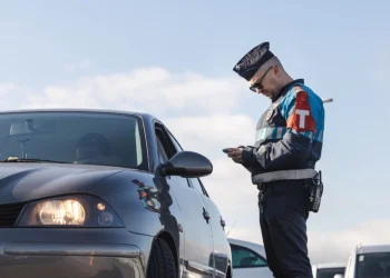 Un agente in divisa della polizia in Portogallo controlla in strada un autovettura alla ricerca di eventuali truffatori, in una giornata dal cielo sereno.