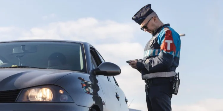 Un agente in divisa della polizia in Portogallo controlla in strada un autovettura alla ricerca di eventuali truffatori, in una giornata dal cielo sereno.