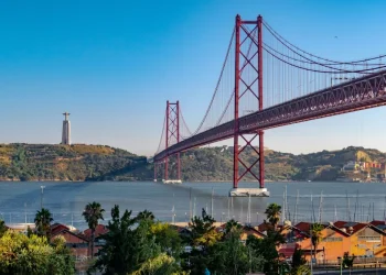Il ponte 25 aprile di Lisbona con lo sfondo del Cristo Rei e il fiume Tejo, sono il confine di applicabilità di Uber Commute. Si vede un cielo azzurro e alcune piante.