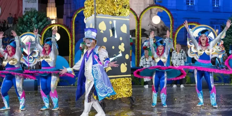 Artisti in costumi colorati ed elaborati, che raffigurano temi come carte da gioco e farfalle, danzano con le braccia alzate davanti a un grande oggetto di carte durante la vivace sfilata notturna di Sant'Antonio Lisbona.