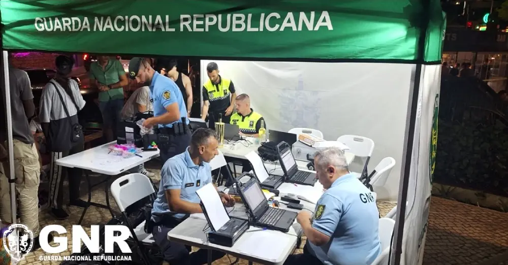 Cinque agenti di polizia si trovano di sotto un gazebo illuminato di notte, svolgendo controlli al pc nel cuore della movida nell'ambito del posto di controllo GNR di Albufeira.
