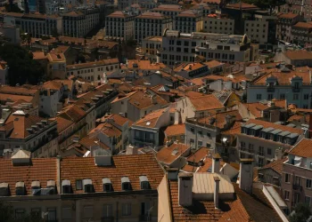 Veduta aerea di Lisbona con edifici ravvicinati con tetti di tegole rosse, camini e strade strette, in Portogallo, dove l'aumento prezzi case sta plasmando la vita urbana alla luce del giorno.
