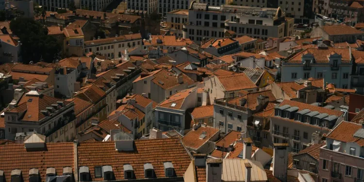 Veduta aerea di Lisbona con edifici ravvicinati con tetti di tegole rosse, camini e strade strette, in Portogallo, dove l'aumento prezzi case sta plasmando la vita urbana alla luce del giorno.