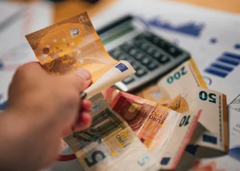 Alcune banconote di euro e una calcolatrice con delle bollette per valutare se è possibile vivere con il salario minimo in Portogallo. Una mano mantiene una banconota da 50 euro.