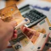 Alcune banconote di euro e una calcolatrice con delle bollette per valutare se è possibile vivere con il salario minimo in Portogallo. Una mano mantiene una banconota da 50 euro.