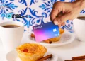 Una mano tiene una carta di credito con logo revolut sullo sfondo di prodotti simbolo del Portogallo, come caffè e pastel de nata e azulejo.