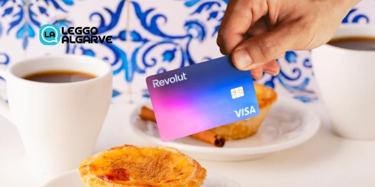 Una mano tiene una carta di credito con logo revolut sullo sfondo di prodotti simbolo del Portogallo, come caffè e pastel de nata e azulejo.