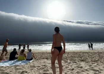 Un folto gruppo di persone osserva delle spettacolari nuvole su una spiaggia in Portogallo. In primo piano una donna in costume di spalle.