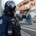Un poliziotto del Portogallo durante un operazione difronte ad una casa probabilmente occupata illegalmente. La scena è di giorno in mezzo ad una strada.