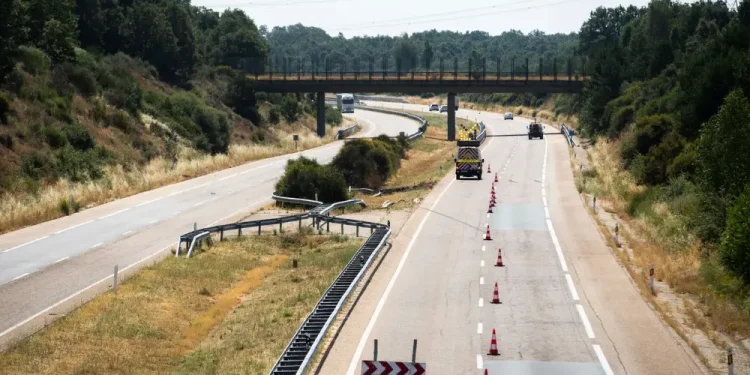 Un'autostrada con una corsia chiusa da coni e barriere, forse a causa dell'incidente di Diogo Jota. I veicoli passano accanto a un guardrail danneggiato, gli alberi costeggiano entrambi i lati della strada e un ponte passa in lontananza.
