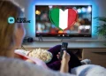 Una donna in Portogallo mentre guardare una tv con bandiera italiana in salotto con un telecomando e dei pop-corn in mano