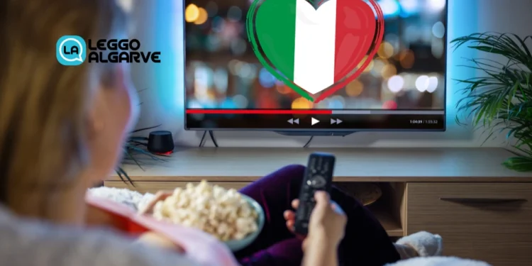 Una donna in Portogallo mentre guardare una tv con bandiera italiana in salotto con un telecomando e dei pop-corn in mano
