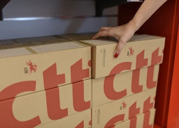 Alcuni pacchi a marchio CTT pronti per gli invii verso gli USA, una mano ne sospende uno.