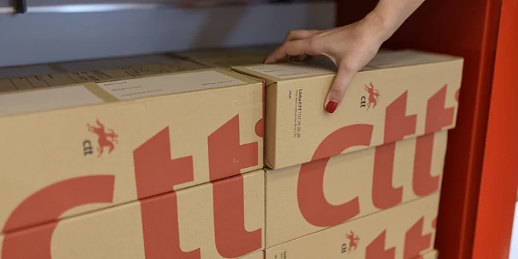 Alcuni pacchi a marchio CTT pronti per gli invii verso gli USA, una mano ne sospende uno.