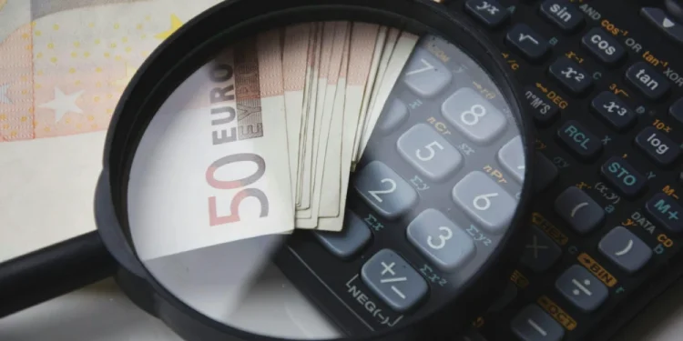 Su un piano bianco una lente di ingrandimento sopra alcune banconote in euro, salario di agosto e settembre, e una calcolatrice per l'IRS.