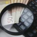 Su un piano bianco una lente di ingrandimento sopra alcune banconote in euro, salario di agosto e settembre, e una calcolatrice per l'IRS.