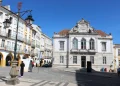 Nella piazza di Evora il palazzo del Banco de Portugal circondato da edifici portoghesi storici con altre banche, una strada non trafficata e alcune persone. Il cielo è sgombro dalle nuvole.