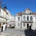 Nella piazza di Evora il palazzo del Banco de Portugal circondato da edifici portoghesi storici con altre banche, una strada non trafficata e alcune persone. Il cielo è sgombro dalle nuvole.