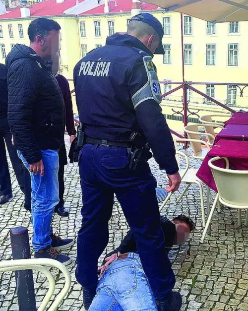 Il momento dell'arresto di un borseggiatore da parte della polizia di Lisbona, si vede un uomo a terra ammanettato e un altro uomo che osserva la scena. Ci sono sullo sfondo dei tavolini di un bar e delle case di colore giallo.