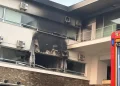 Un edificio con pareti annerite e un grande foro bruciato dall'incendio RSA Mirandela, con finestre rotte. Sono attaccate diverse unità di condizionamento e sulla destra è visibile parte di un veicolo di emergenza rosso.