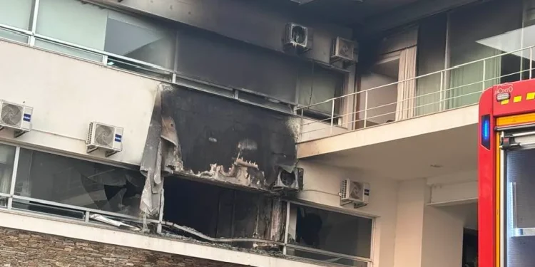 Un edificio con pareti annerite e un grande foro bruciato dall'incendio RSA Mirandela, con finestre rotte. Sono attaccate diverse unità di condizionamento e sulla destra è visibile parte di un veicolo di emergenza rosso.