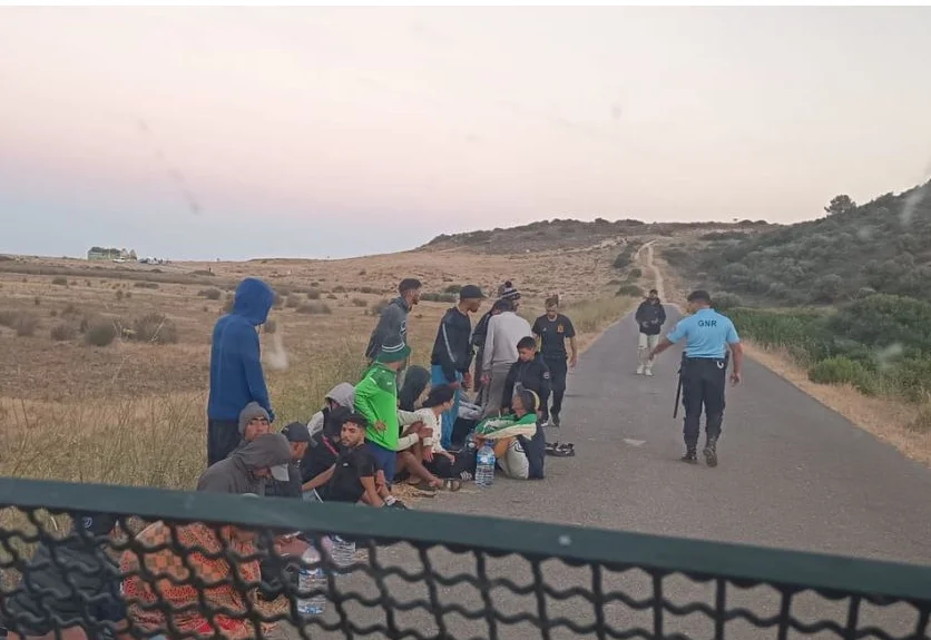 Lungo una strada dell'Algarve alcuni migranti protagonisti dello sbarco a Vila do Bisto ricevono indicazioni da un poliziontto della GNR.