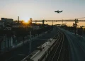 Un treno che viaggiare sui binari in Europa ed un aereo nel cielo al tramonto che sta atterrando verso i palazzi dell'aeroporto.