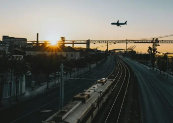 Un treno che viaggiare sui binari in Europa ed un aereo nel cielo al tramonto che sta atterrando verso i palazzi dell'aeroporto.