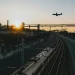 Un treno che viaggiare sui binari in Europa ed un aereo nel cielo al tramonto che sta atterrando verso i palazzi dell'aeroporto.