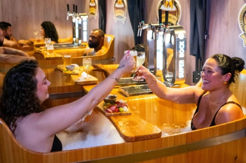 Due donne brindano all'interno della Beer & Wine SPA a Lisbona caratterizzato da vasche in legno con rubinetti per la birra, insegne decorative e luci soffuse, che creano un'atmosfera calda e invitante.