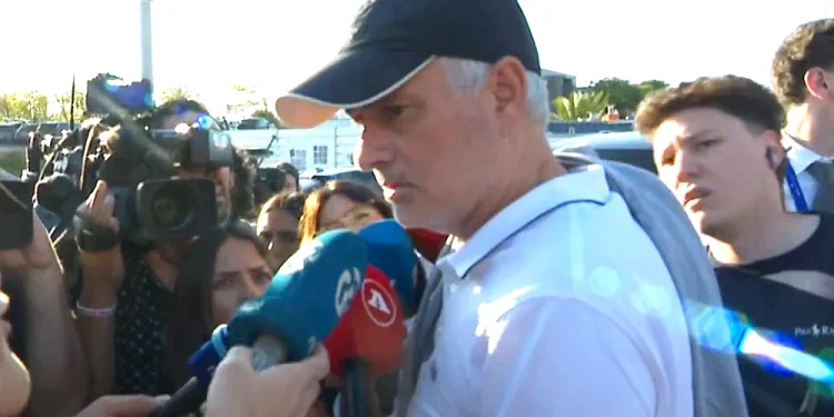 Jose Mourinho con cappellino nero e polo bianca rilascia un intervista come nuovo allenatore del Benfica, ci sono alcuni giornalisti e telecamere attorno a lui mentre parla in alcuni microfoni colorati.