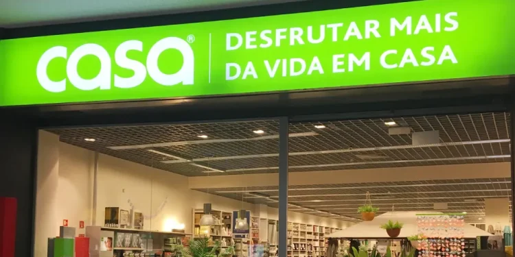 La vetrina con l'insegna verde "casa DESFRUTAR MAIS DA VIDA EM CASA" sovrasta un interno luminoso che espone articoli per la casa e oggetti d'arredamento, poco prima della chiusura del negozio CASA.