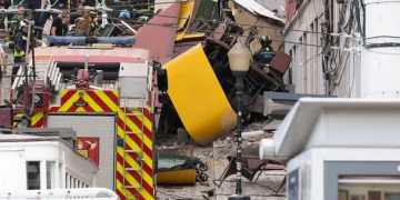 I vigili del fuoco intervengono sulla scena dell'incidente della funicolare di Lisbona da Gloria, che è deragliata e si è schiantata contro dei palazzi. I detriti sono sparsi mentre arrivano i mezzi di soccorso e i curiosi osservano dall'alto e di lato, chiedendosi cosa sia successo.