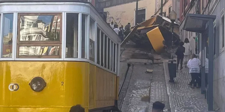 La funicolare di Lisbona e diverse persone si trovano in fondo a una strada stretta, dove una funicolare deragliata è precipitata e si è ribaltata davanti a noi, bloccando i binari. I detriti sono sparsi mentre gli astanti osservano il malfunzionamento e attendono la manutenzione.