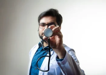 Un medico di famiglia privato in Portogallo con camice bianco e camicia azzurra mostra uno stetoscopio.