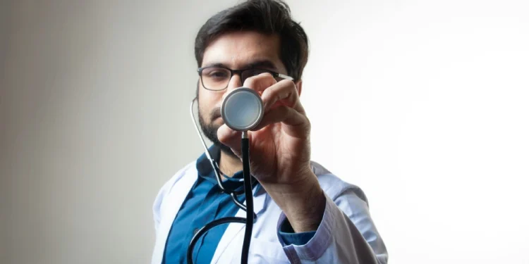 Un medico di famiglia privato in Portogallo con camice bianco e camicia azzurra mostra uno stetoscopio.