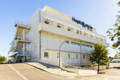 Edificio moderno del ospedale Lusiadas di Albufeira, con la strada di accesso che gli gira attorno a alcune piante.